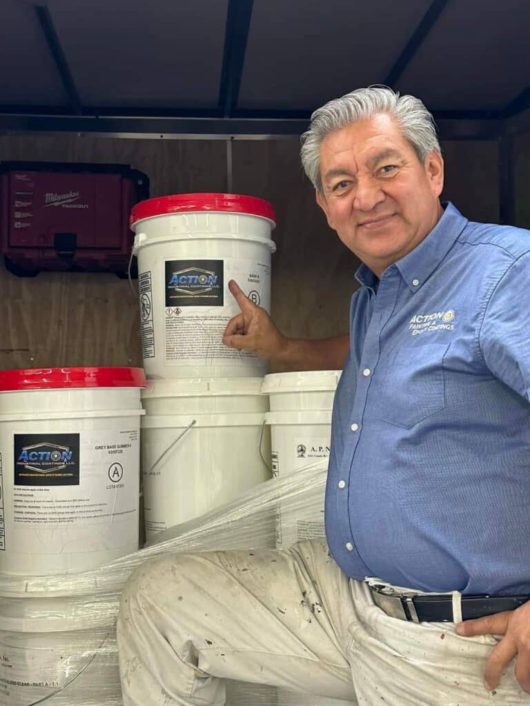 Man pointing to Action Industrial Coatings epoxy product buckets inside a work trailer.