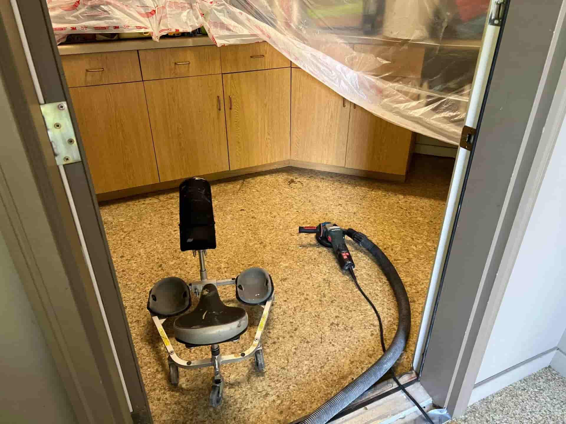 Small edge grinder and vacuum hose set up for interior concrete floor preparation in a room with protected cabinets.