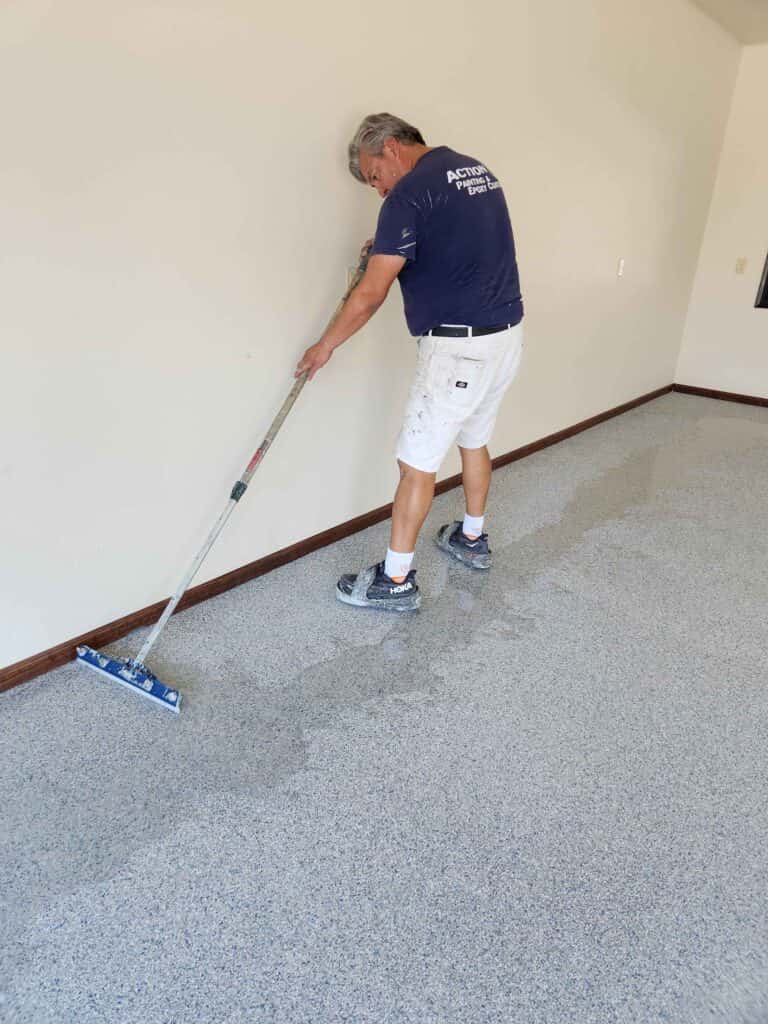 Installer using a long-handled floor squeegee to spread an epoxy coating in a residential garage.
