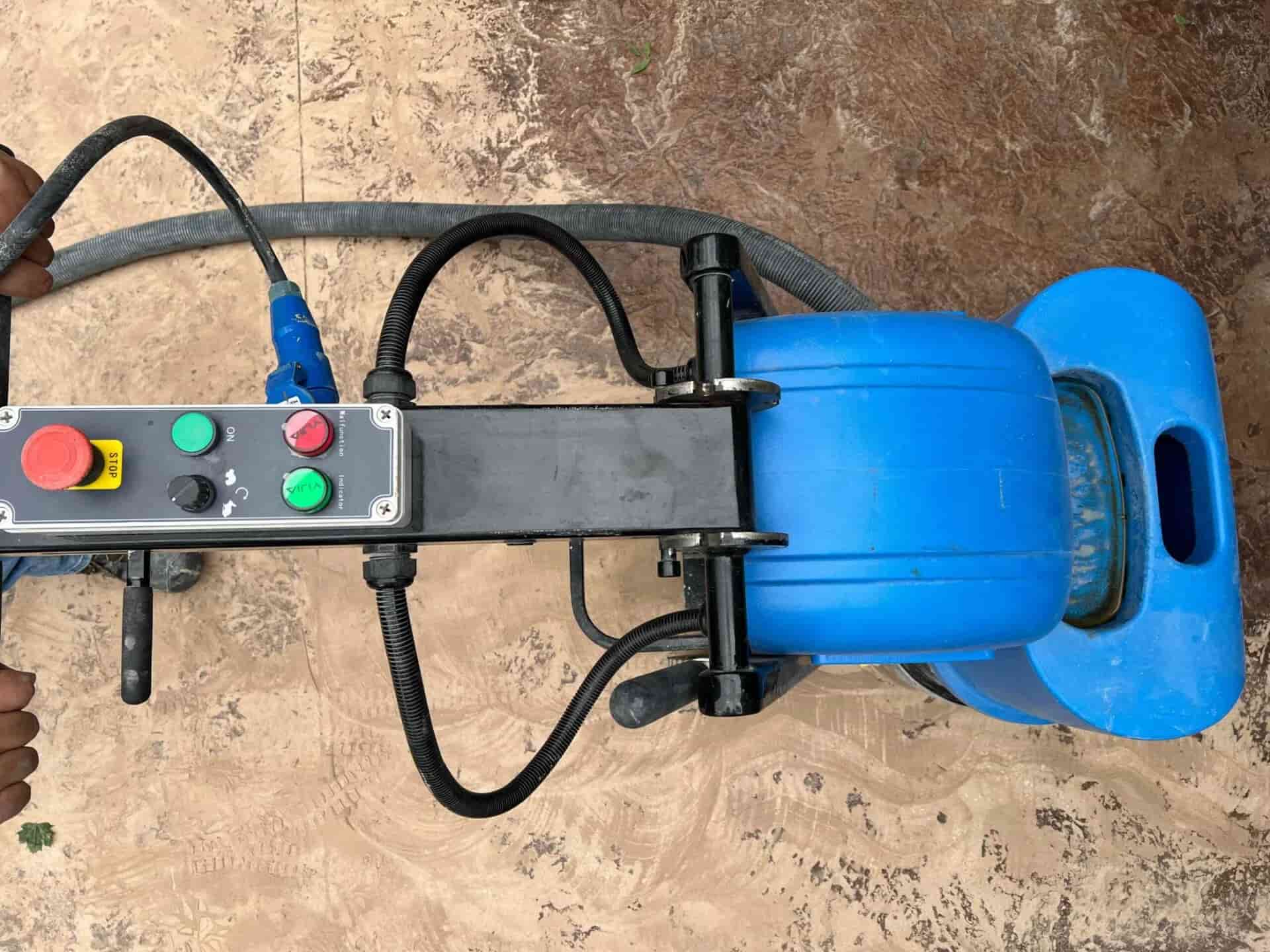 Top-down view of a handheld concrete floor grinder with control panel and vacuum hose used for surface preparation.