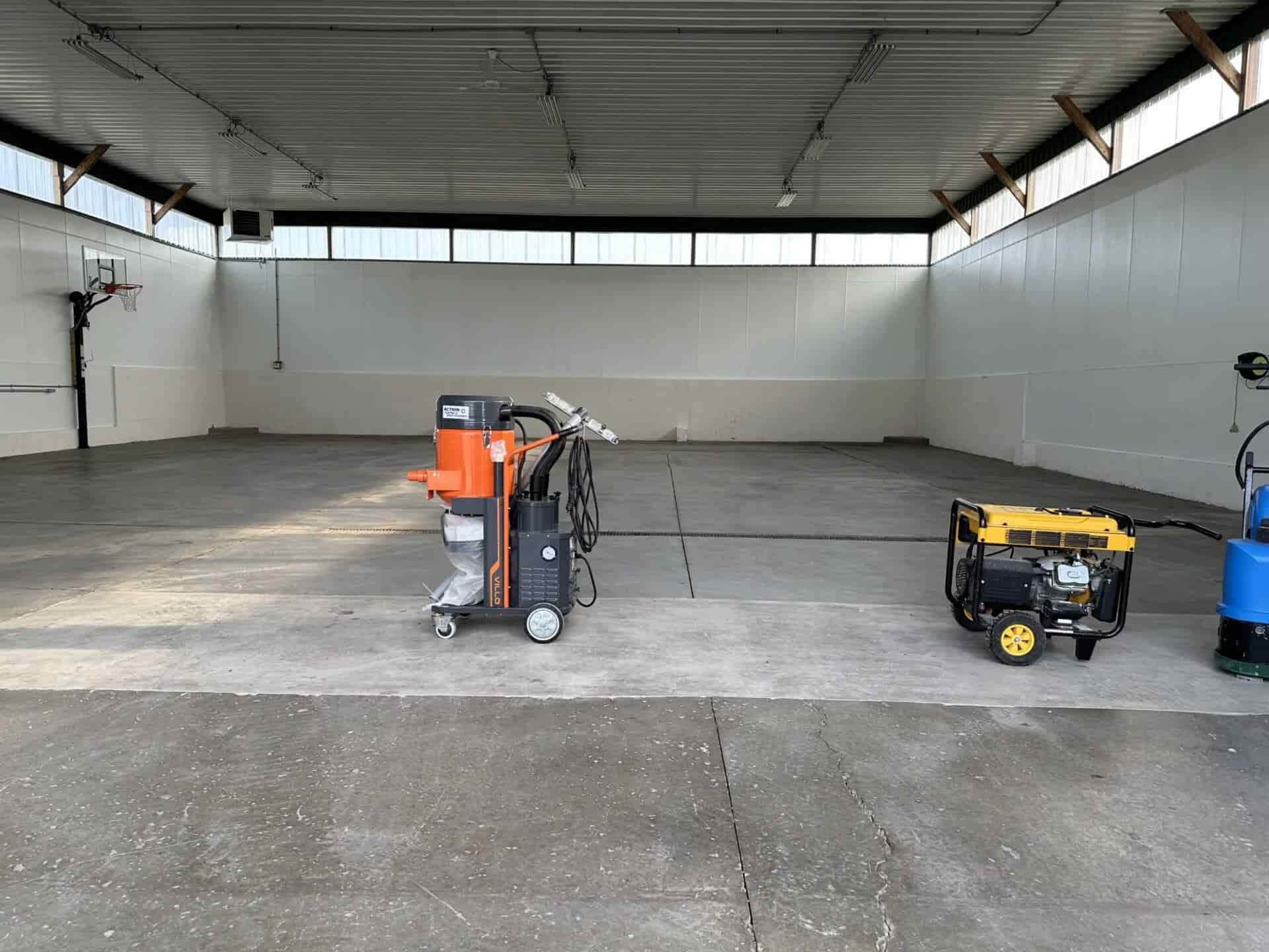 Concrete floor preparation equipment staged in a large interior space, including grinder, dust-control vacuum, and portable generator for jobsite power.